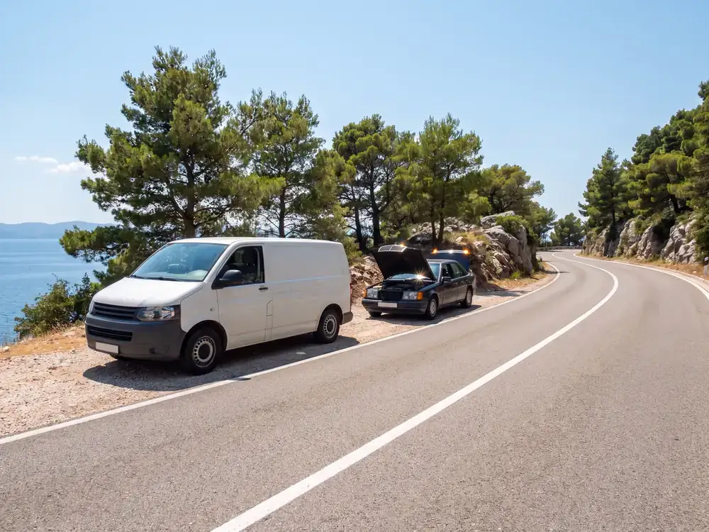 Servisno vozilo uz automobil s podignutom haubom na obalnoj cesti