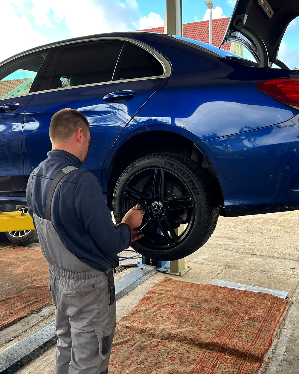 Mechanic tightening a wheel on a blue Mercedes raised on the workshop lift